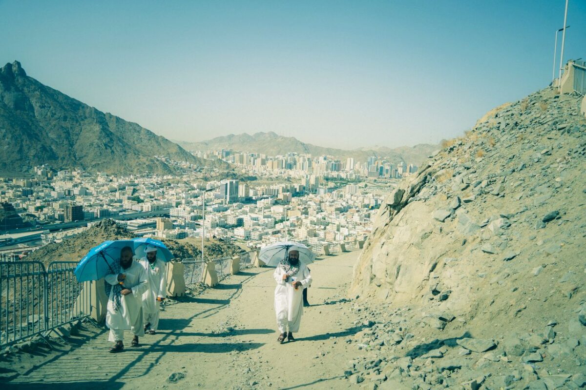 Pilgrims climb a rocky path in Makkah, Saudi Arabia, with the cityscape in view.